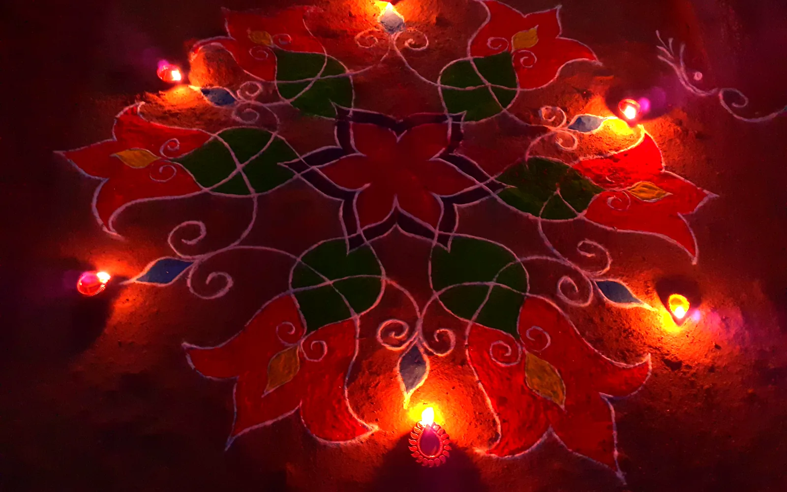 Clay diyas glowing around a red and green flower rangoli on Diwali night
