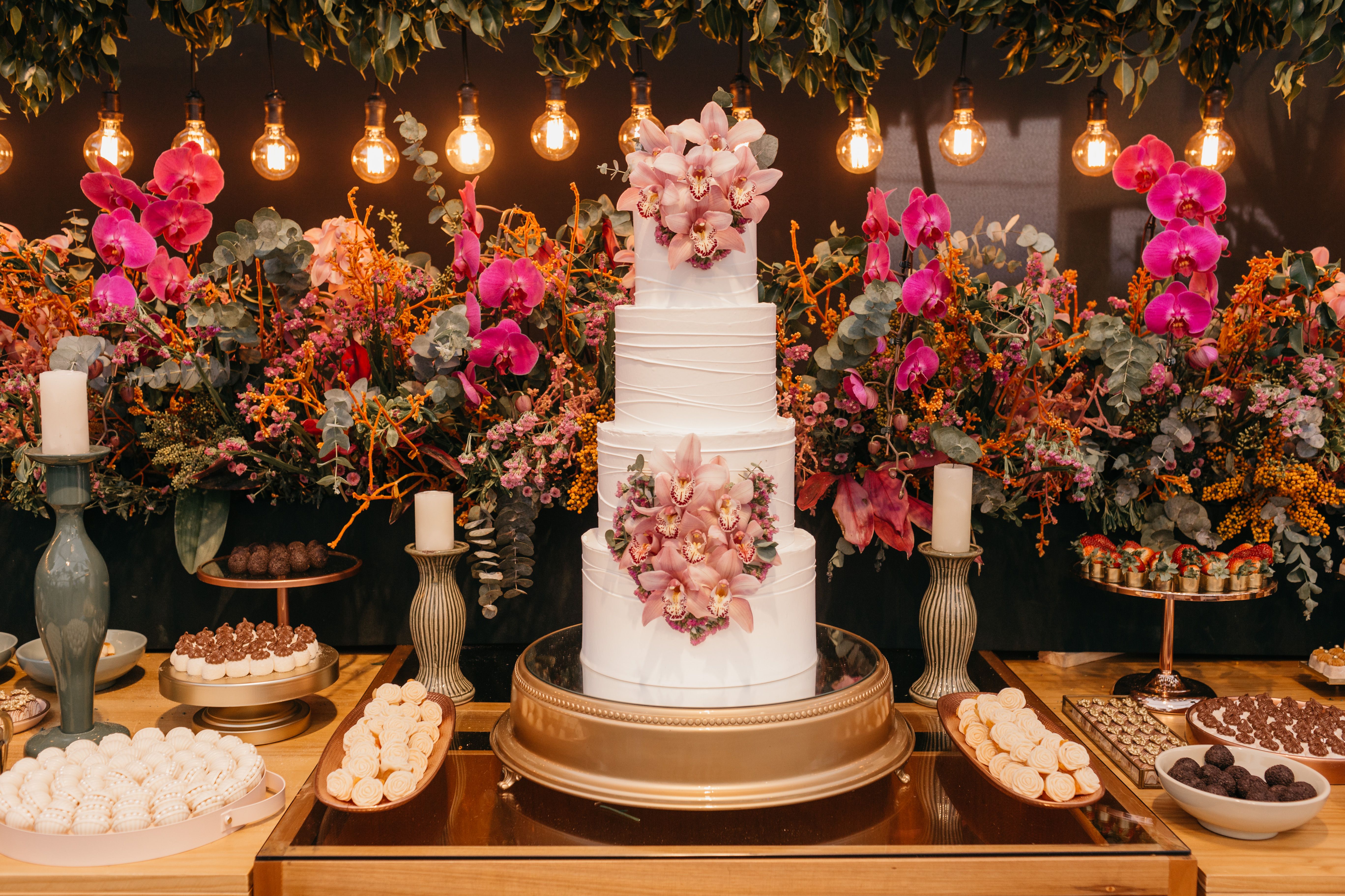 A three-tier white celebration cake on a stand beside stacked dessert plates at a reception.