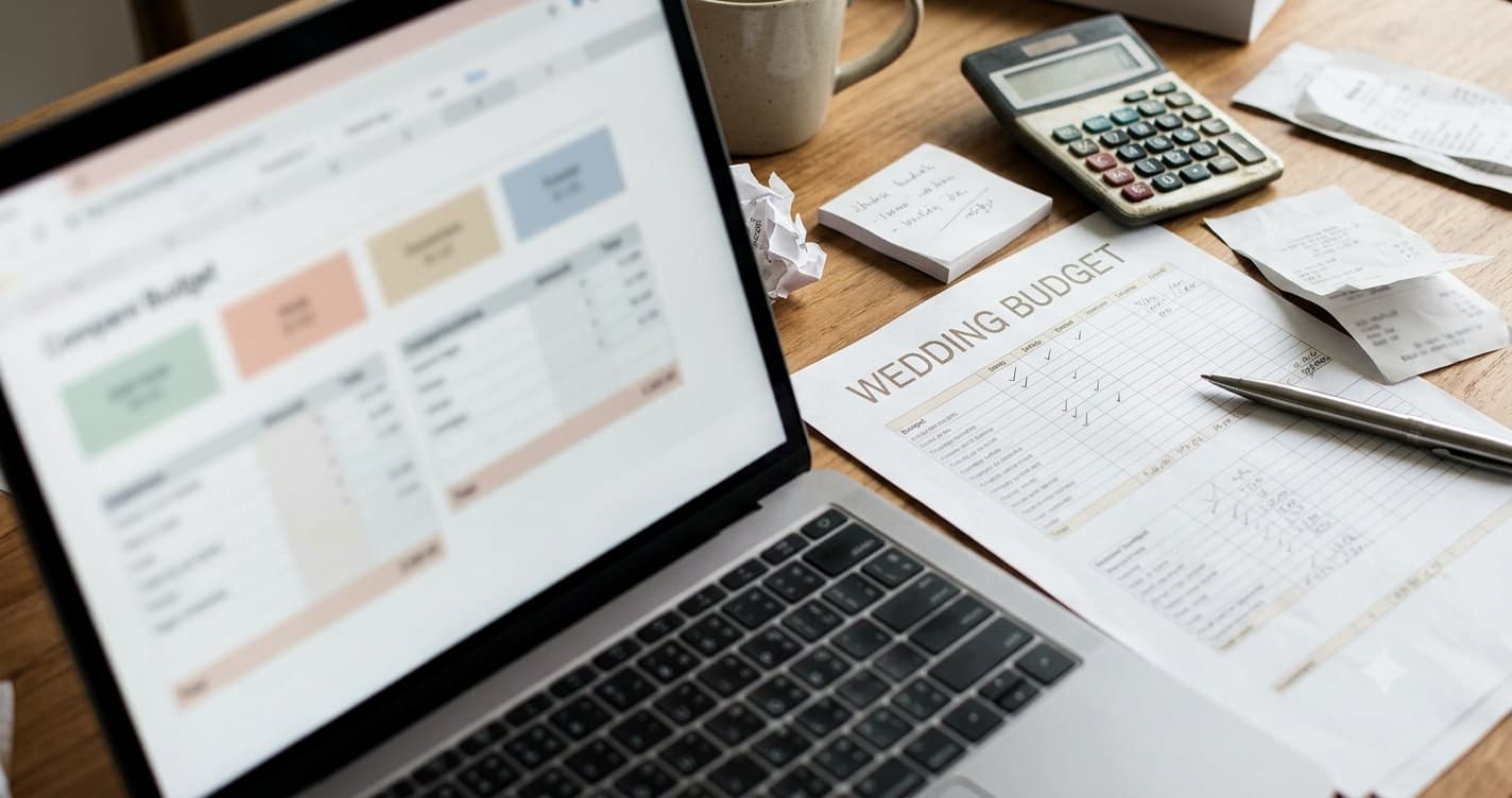 Close-up of a wedding insurance quote on a laptop screen next to a calculator and a wedding budget spreadsheet