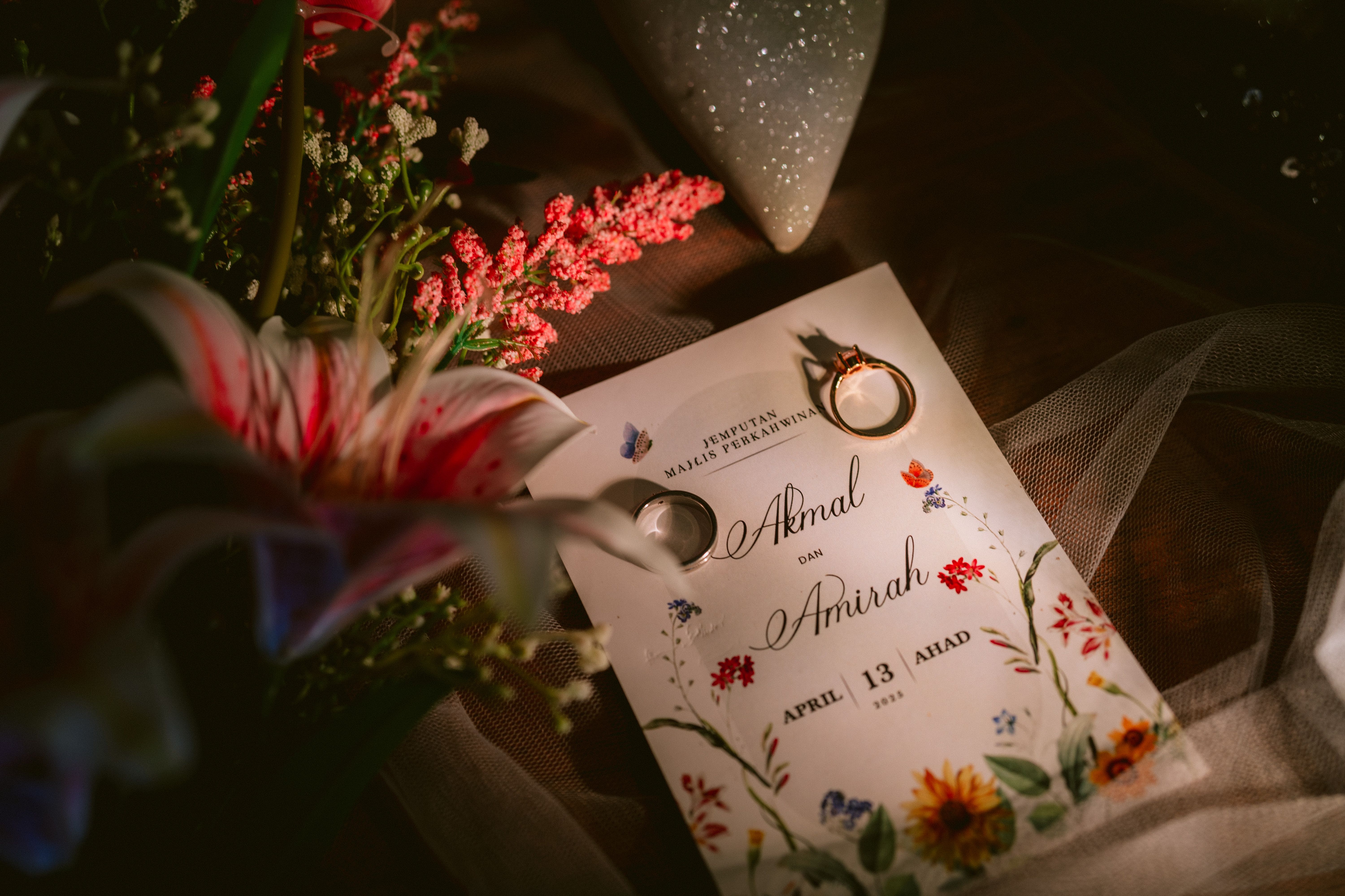 An Indian wedding card with gold foil detailing next to a phone showing a digital invitation, on a decorated table.